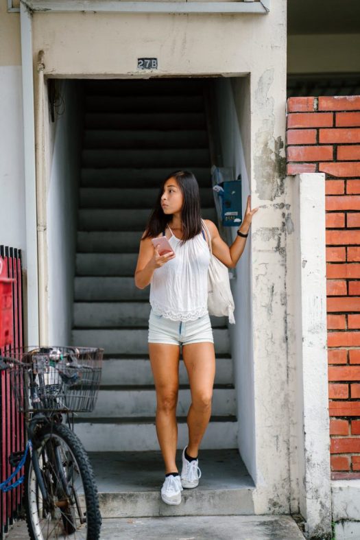 a person wearing shorts and a tank top walks down stairs to the street. she is holding a phone.