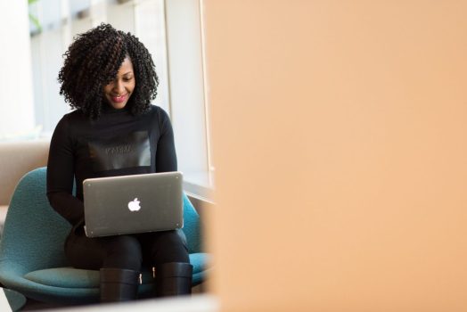 a woman sits smiling at her laptop