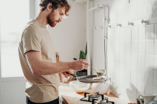 a man cooks something over a stove in a kitchen with white tile