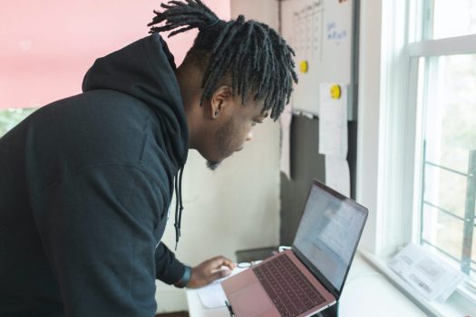 a man with dreadlocks leans over a laptop