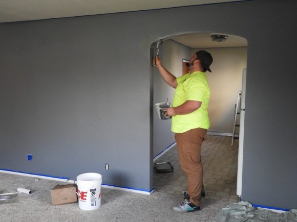 a man in a neon yellow shirt paints a wall in a house undergoing renovation