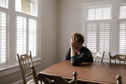 a person sits at a dining table and holds their head with one hand in distress