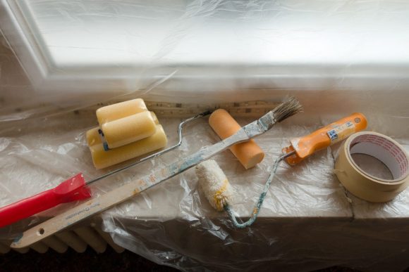 a plastic covered windowsill holds paintbrushes, tape, and a paintroller