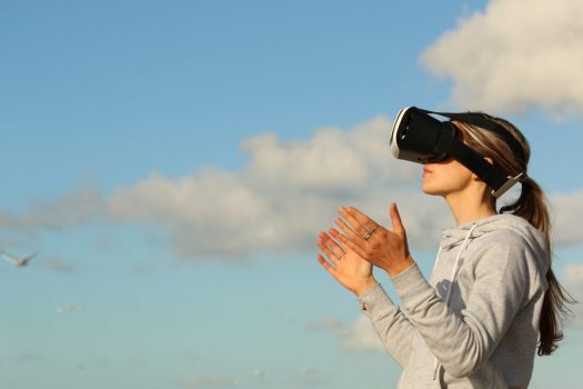 a person in a ponytail wears a virtual reality headset in front of a blue sky with clouds
