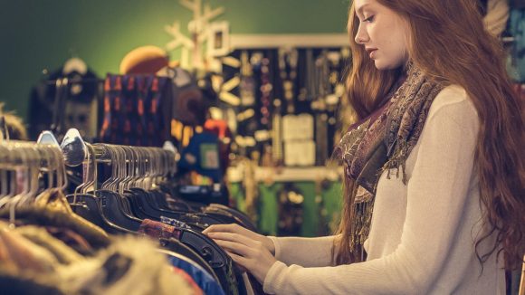 A young woman looks at clothing hanging on a rack in a thrift store